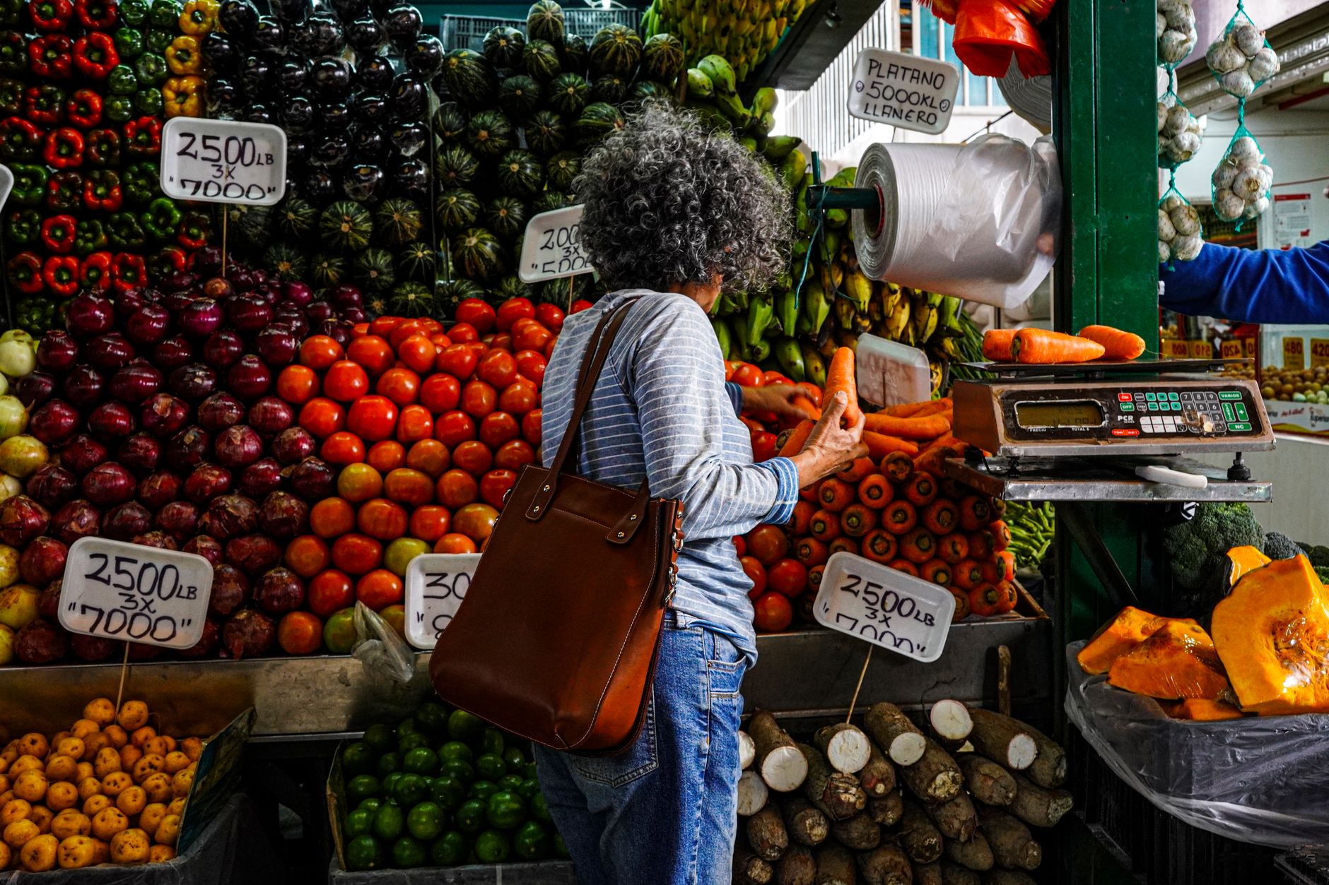 Mujer comprando en un vibrante puesto de mercado local lleno de frutas y verduras frescas.