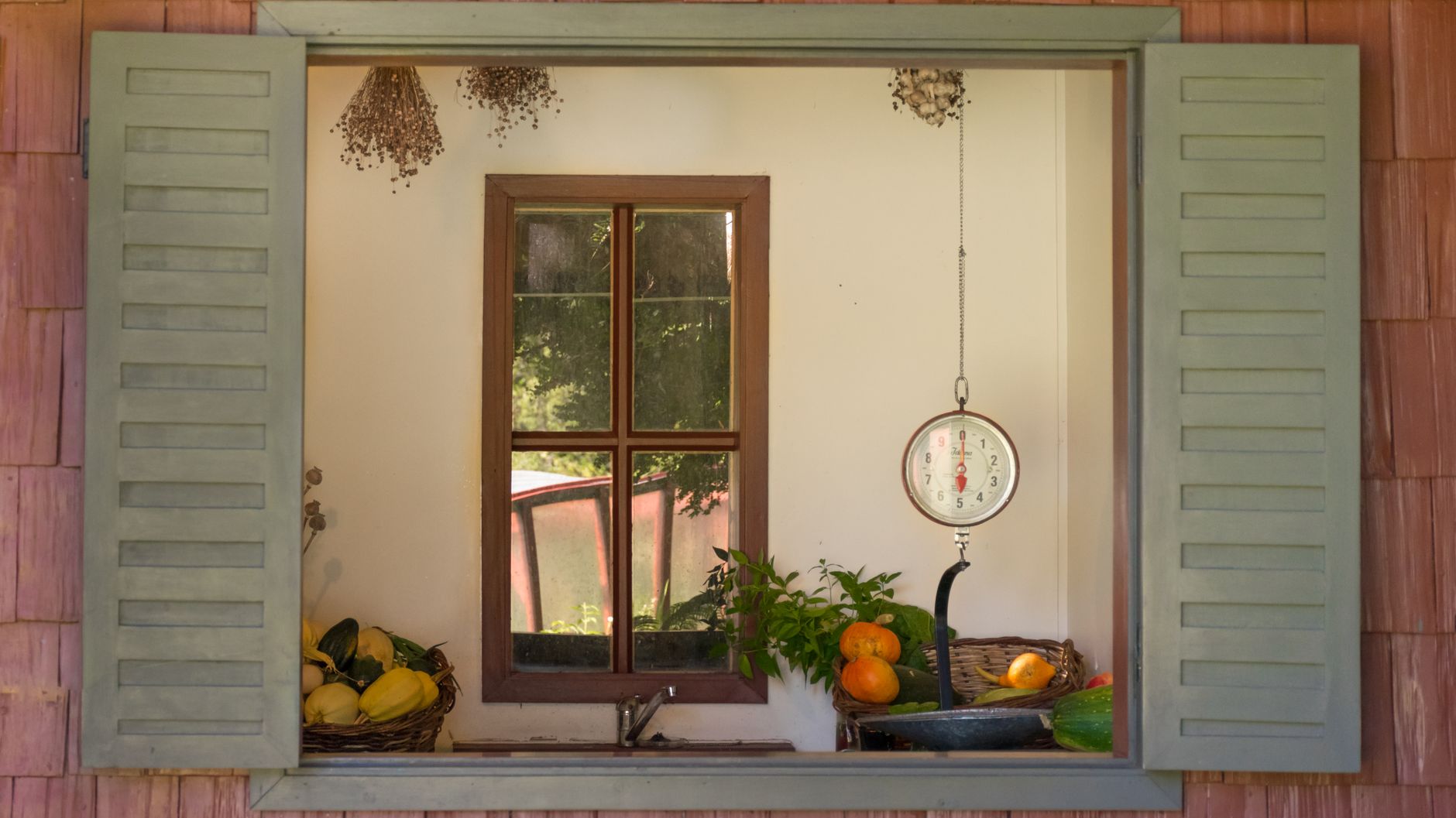 Escena rústica de cocina a través de la ventana con báscula, frutas y hierbas, que exuda encanto vintage.
